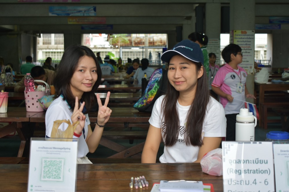 Two MessageSpring teammates smiling at a school event registration desk, one in a MessageSpring cap
