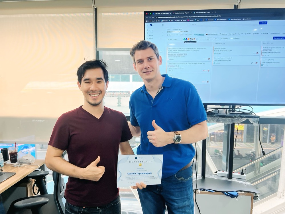 A teammate holding his promotion certificate beside a colleague giving a thumbs-up